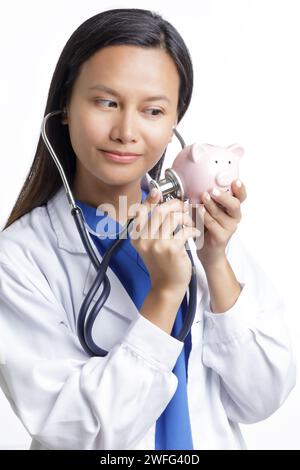 Asiatische amerikanische Ärztin untersucht eine Schweinebank, Konzept zeigen die hohen Kosten der Gesundheitsversorgung isoliert auf einem weißen Hintergrund mit Kopierraum Stockfoto