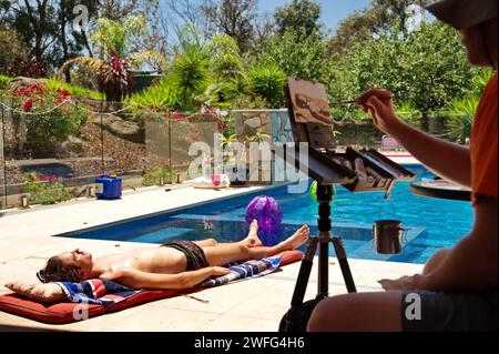 Maler, der einen jungen Mann am Rand des Schwimmbades anmalt Stockfoto