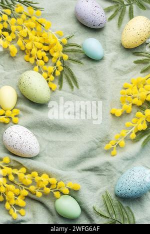 Bunte ostereier und Mimosa-Blumen auf grünem Textil-Hintergrund. Draufsicht mit Kopierbereich Stockfoto
