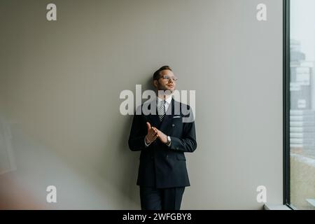 Nachdenklicher junger Geschäftsmann, der sich im Büro an eine graue Wand lehnt Stockfoto