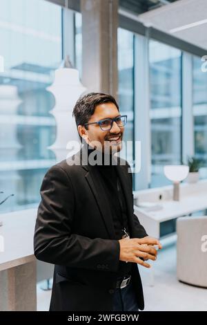 Lächelnder junger Geschäftsmann, der während der Konferenz in Business-Casual steht Stockfoto
