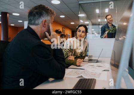 Geschäftsfrau diskutiert mit reifem Geschäftsmann, der am Schreibtisch im Büro sitzt Stockfoto