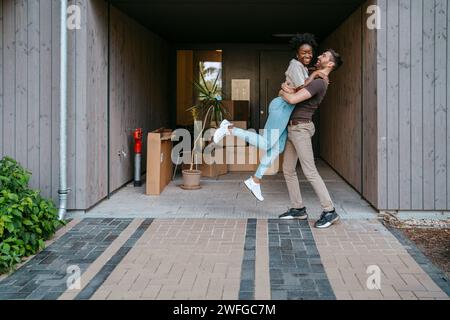 Glückliches multirassisches Paar, das Spaß beim Stehen am Gebäudeeingang hat Stockfoto
