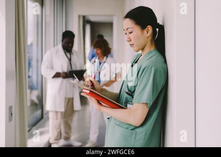 Seitenansicht einer Arztschreiberin auf Klemmbrett im Krankenhauskorridor Stockfoto