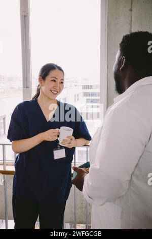 Lächelnde Krankenschwester, die eine Kaffeetasse hält, während sie im Krankenhaus zum Arzt schaute Stockfoto
