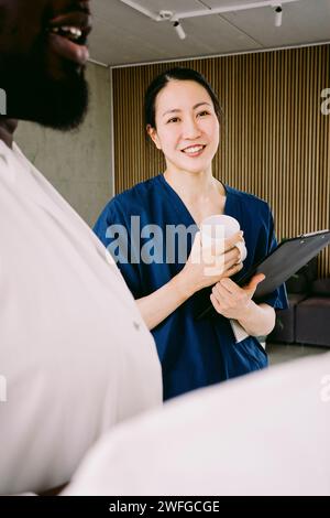 Lächelnde Krankenschwester, die Kaffeetasse hält, während sie beim männlichen Arzt im Krankenhaus steht Stockfoto