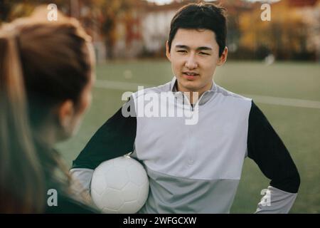 Männlicher Athlet, der mit weiblicher Trainerin spricht, während er auf dem Sportplatz steht Stockfoto