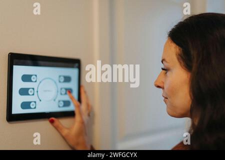 Reife Frau, die ein digitales Tablet für die Temperaturregelung zu Hause verwendet Stockfoto