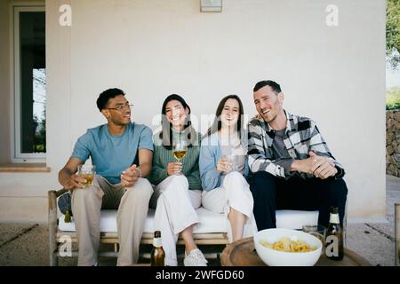 Fröhliche männliche und weibliche Freunde mit Drinks auf dem Sofa im Hinterhof Stockfoto