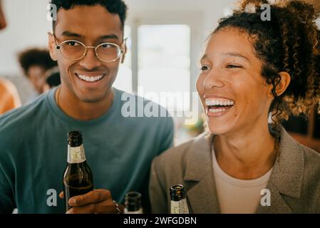 Fröhlicher junger Mann und Frau mit Bierflaschen in der Küche Stockfoto