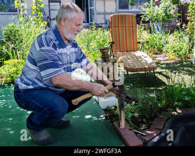 Ein grauhaariger Mann und ein Samovar. Ein Mann hackt Holzspäne für einen Samovar im Garten. Tee im Garten im Samovar. Stockfoto