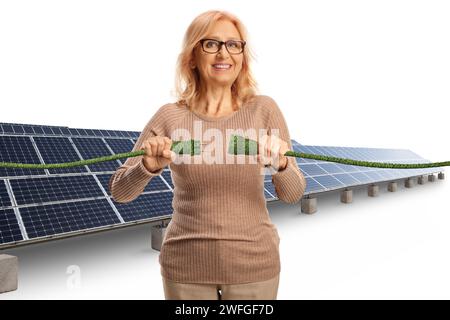 Lächelnde reife Frau auf einem Solarfeld, die grüne elektrische Kabel auf weißem Hintergrund steckte Stockfoto