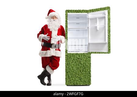 Santa claus lehnt sich auf einen grünen Kühlschrank isoliert auf weißem Hintergrund, nachhaltige Elektrogeräte Stockfoto