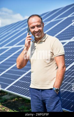 Glücklicher Geschäftsmann, der einen wichtigen Anruf hat. Ein Mann, der über seine Investition in alternative Energiequellen spricht. Mann, der auf dem Hintergrund von Solarpaneelen telefoniert. Stockfoto