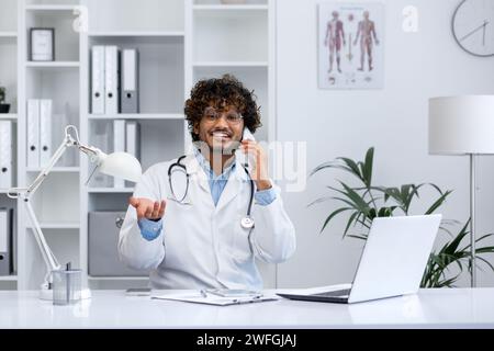 Fröhliche Beratung durch medizinisches Fachpersonal am Telefon, umgeben von medizinischen Geräten in einem gut beleuchteten Klinikbüro. Stockfoto