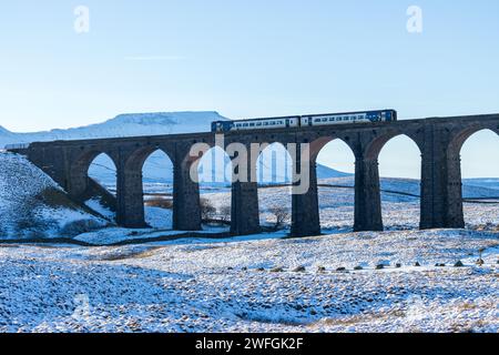 Ein nördlicher Zug überquert den berühmten Ribblehead Viaduct an einem winterlichen Tag in den Yorkshire Dales, mit schneebedecktem Ingleborough im Hintergrund Stockfoto