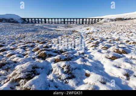 Der Ribblehead Viaduct im Winter in den Yorkshire Dales, mit viel Schnee auf dem Boden und dramatischer Bergkulisse. An einem sonnigen Tag aufgenommen. Stockfoto