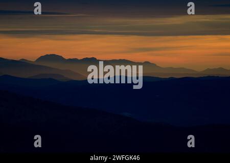 Sonnenuntergang über geschichteten Bergketten mit nebeligen Tälern, die den atmosphärischen Effekt und den Farbverlauf der Dämmerung einfangen. Stockfoto