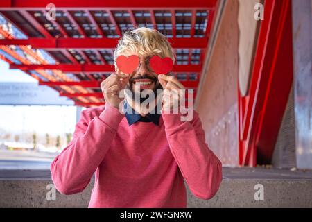 Porträt glücklicher junger Mann in Liebe, der ihre Augen hinter Papierherzen versteckt. Liebende Stockfoto