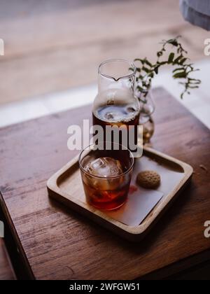 Handgegossener Kaffee kalt Brühen Sie Espresso-Eiskaffee mit Eiswürfeln. Glas Kaltgebrühter Kaffee mit Eis auf Morgen hellen Holztisch Hintergrund. Stockfoto