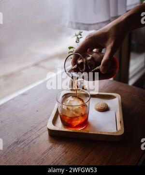 Handgegossener Kaffee kalt Brühen Sie Espresso-Eiskaffee mit Eiswürfeln. Glas Kaltgebrühter Kaffee mit Eis auf Morgen hellen Holztisch Hintergrund. Stockfoto