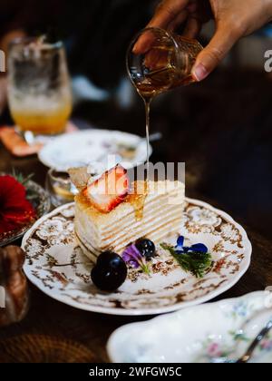 Kreppkuchen Backstück mit Erdbeeren- und Honigsauce auf Holztisch. Schließen Sie ein Stück Erdbeerkreppenkuchen auf einem weißen Teller mit Erdbeerfrüchten Stockfoto