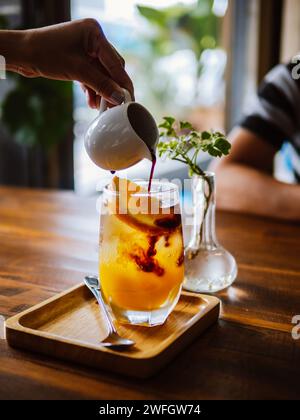 Kalter, erfrischender Kaffee mit frisch gepresstem Orangensaft, Espresso und Eis in der Zubereitung. Gießen Sie schwarzen Kaffee in das Glas gefüllt mit Stockfoto