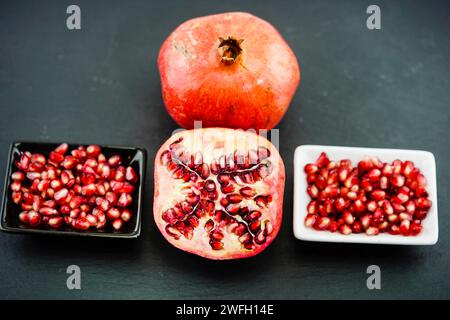 Granatapfel, anar (Punica granatum), Granatäpfel, eine Hälfte, Granatapfelkerne in einer Schüssel Stockfoto