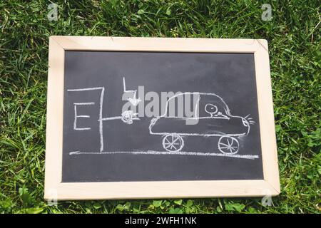 Schwarze Tafel mit einem gezogenen Elektroauto an einer Ladestation, Symbolbild Stockfoto