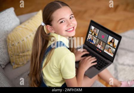 Lächelnde Schülerin, die zu Hause auf der Couch sitzt und einen Laptop benutzt Stockfoto