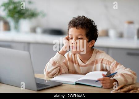 Kleiner schwarzer Junge, der sich müde und schläfrig fühlt, während er seine Hausaufgaben macht Stockfoto