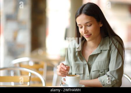 Nachdenkliche Frau, die Kaffee rührt, sitzt auf einer Bar-Terrasse Stockfoto