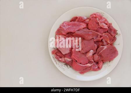 Fleisch auf einer Keramikschale auf beigefarbenem Hintergrund. Rohes Rindfleisch zum Kochen. Draufsicht. Stockfoto