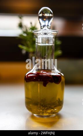 Eine klare Glaskruete gefüllt mit goldenem Olivenöl und einem Zweig Kräuter, perfekt zum Dressing. Stockfoto