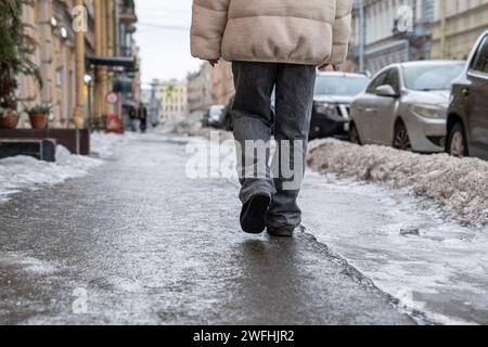 Person, die auf rutschigem Bürgersteig läuft, Rückansicht. Asphalt bedeckt mit rutschigem Eis, gefrorenem Regen. Stockfoto