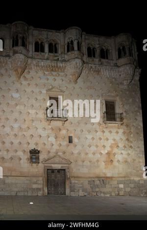 Altes, strukturiertes Gebäude mit zwei Balkonen und einer Holztür, beleuchtet bei Nacht, strahlt ein historisches Ambiente aus. Stockfoto