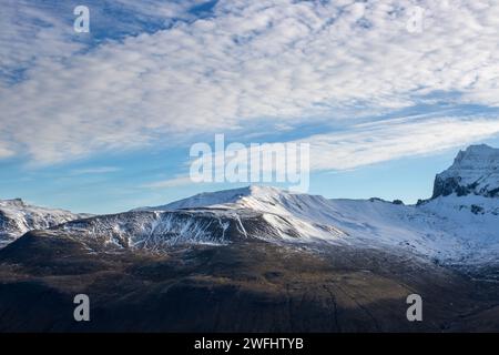 Blick aus einem Tal, umgeben von Bergen mit einer leichten Schneeschicht. Blauer Himmel mit strukturierten weißen Wolken. Borgarfjordur, Nordosten Islands. Stockfoto