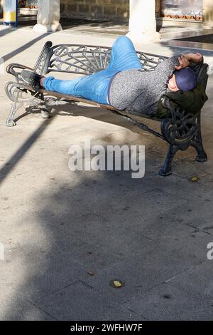 Städtische Erholung, nicht erkennbare Person auf einer öffentlichen Bank... Person, die sich auf einer Parkbank entspannt und die Sonne genießt. Stockfoto