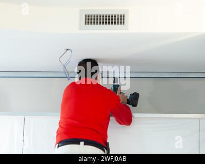 Ein Arbeiter aus Gipskarton installiert eine Gipskartonwand an den Küchenschränken, um das Absaugrohr der Haube abzudecken. Stockfoto