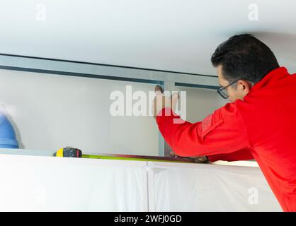 Ein Arbeiter aus Gipskarton installiert eine Gipskartonwand an den Küchenschränken, um das Absaugrohr der Haube abzudecken. Stockfoto