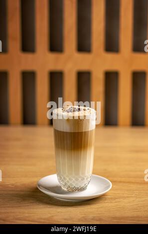 Glas leckerer Latte Macchiato mit Milchschaum und kleinen Schokoladenkugeln in transparentem Glasbecher Stockfoto