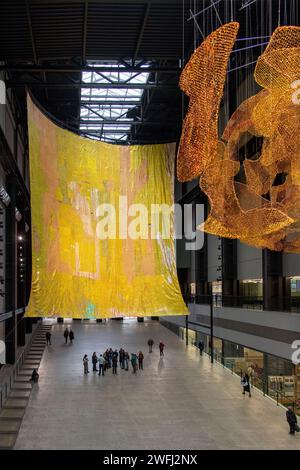 London, UK-12. Dezember 2023; Turbine Hall of Tate Moderne Kunstgalerie mit Kunstwerken von kaskadierenden Metallhängen hinter dem Roten Mond des Künstlers El Anatsu Stockfoto