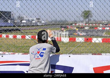 Junger Pilot, der sich ins Netz lehnt und Renntests auf der Gokart-Strecke beobachtet Stockfoto