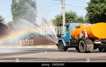 Truck streut Wasser auf die Straße vor einem Regenbogenhintergrund. Städtische Pflegedienste. Stockfoto