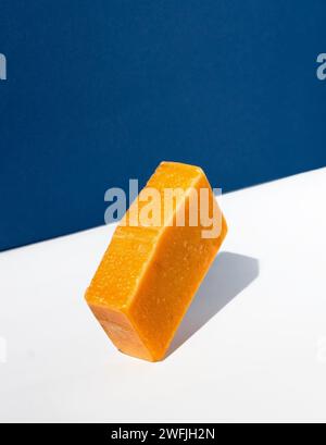 Orangefarbene Seifenleiste auf weiß-blauem Hintergrund. Kreatives Konzept der handgemachten Kosmetik aus Naturprodukten. Stockfoto