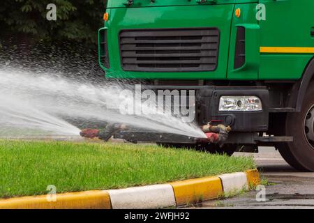 Nahaufnahme des Trucks streut Wasser auf das grüne Gras. Städtische Pflegedienste. Stockfoto