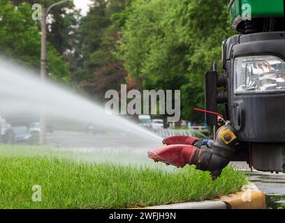 Nahaufnahme eines kommunalen Lastwagens, der den Rasen auf den Straßen bewässert. Stockfoto
