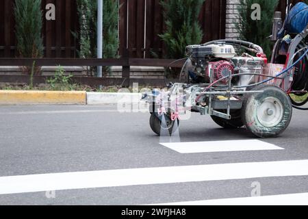 Stadtarbeiter malen Straßenübergangsspuren. Lackiermaschine lackiert Streifen auf Asphalt für Fußgänger. Stockfoto