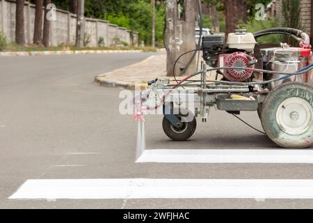 Stadtarbeiter malen Straßenübergangsspuren. Lackiermaschine lackiert Streifen auf Asphalt für Fußgänger. Stockfoto