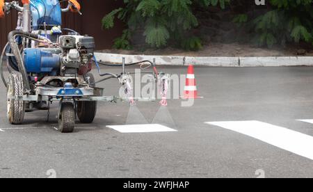 Stadtarbeiter malen Straßenübergangsspuren mit Malmaschine. Stockfoto